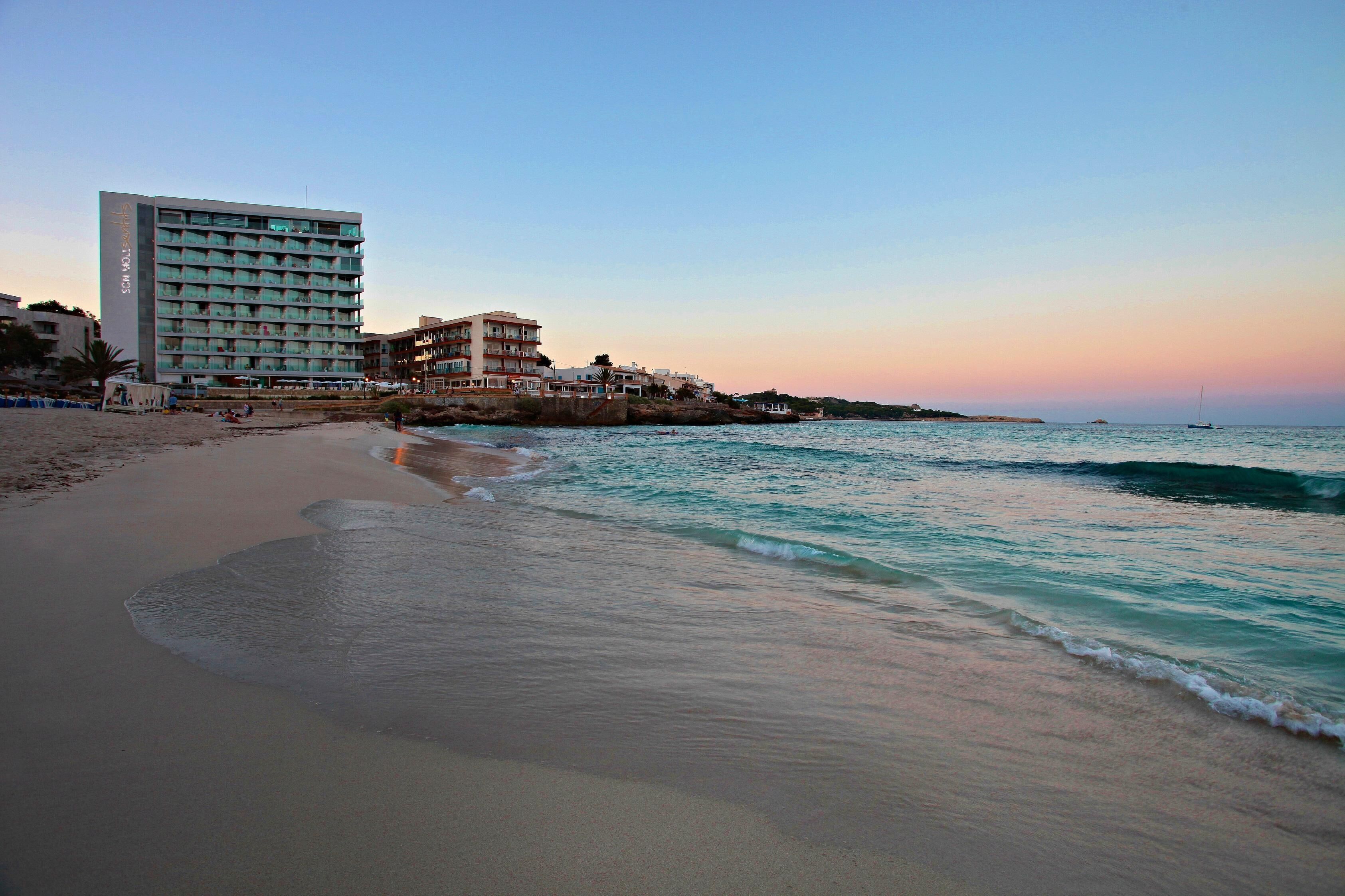 Un hotel frente a la playa con varios pisos, una playa de arena y un mar tranquilo.