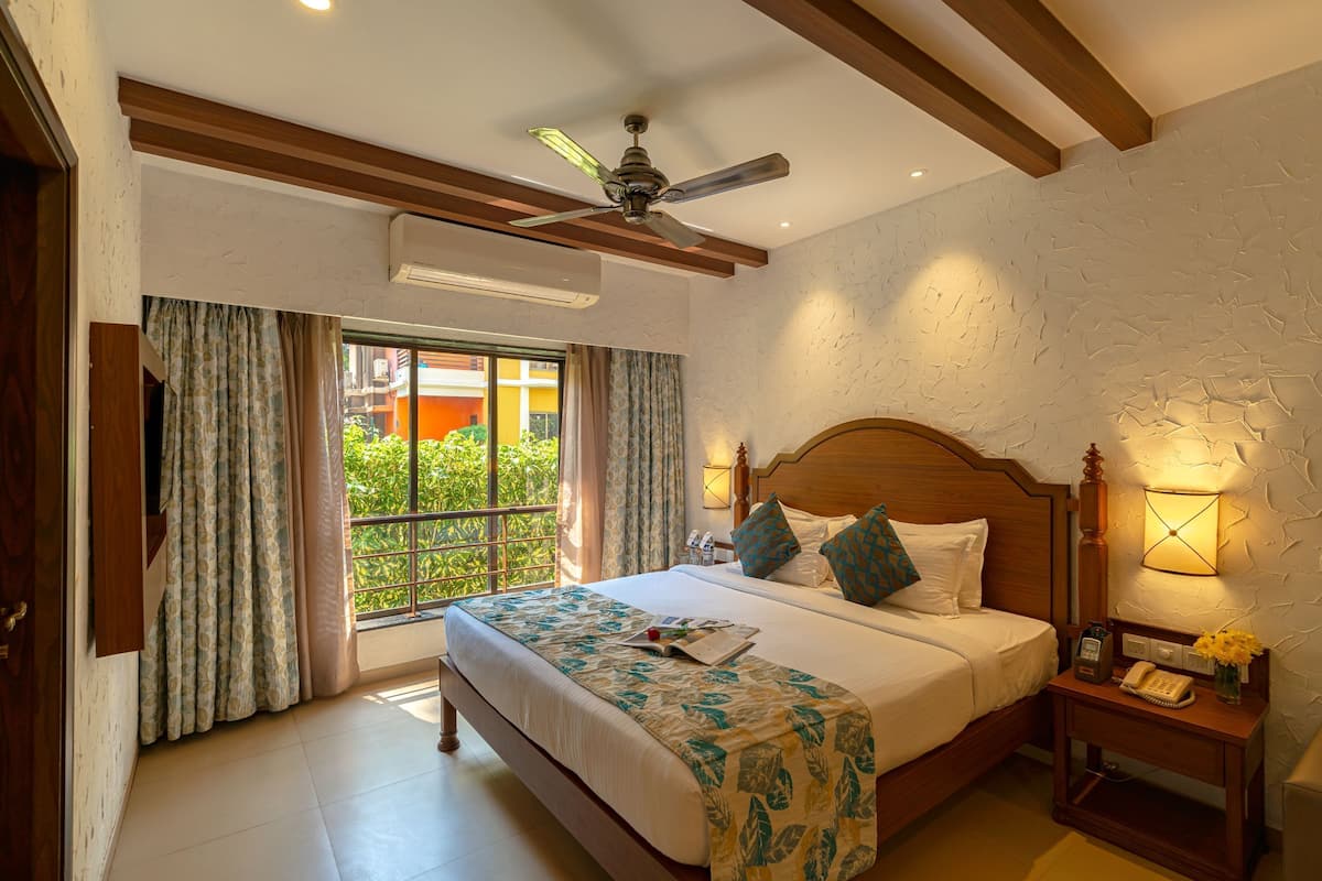 A hotel room with a bed, a bedside table, a nightstand, a ceiling fan, and a window with curtains.