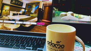 Een laptop waarop een hotelwebsite wordt getoond, een koffiemok met de tekst 'adamo hospitality', en een kleurrijk tijdschrift of brochure.