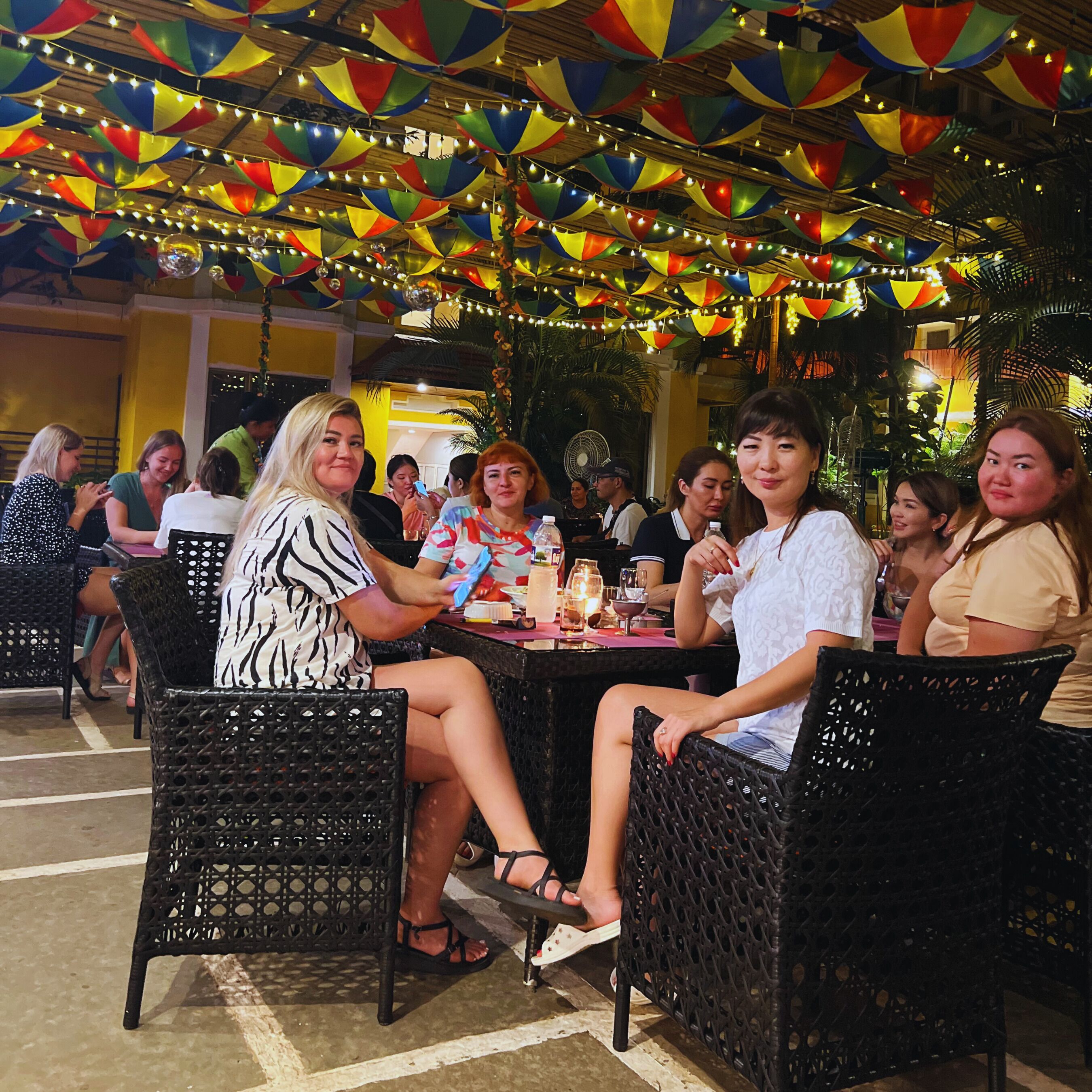 An outdoor dining area with wicker chairs and tables, decorated with colorful triangular flags and string lights.