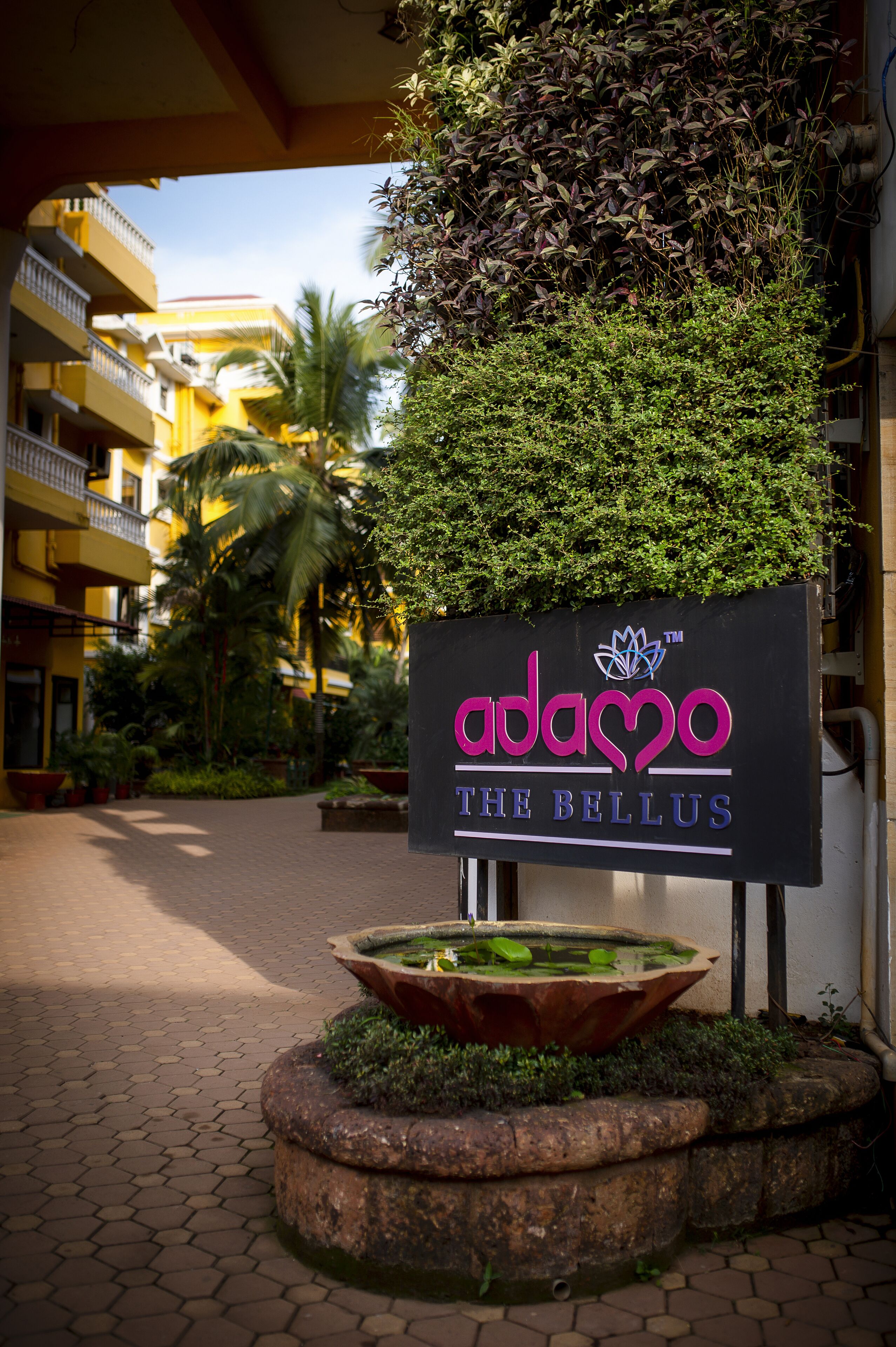 A hotel sign with a logo and name, surrounded by a landscaped area with a water feature and potted plants.