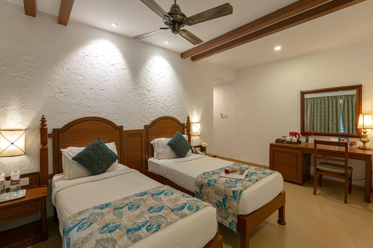 Une chambre d’hôtel avec deux lits, un bureau, une chaise, un ventilateur de plafond et un miroir.