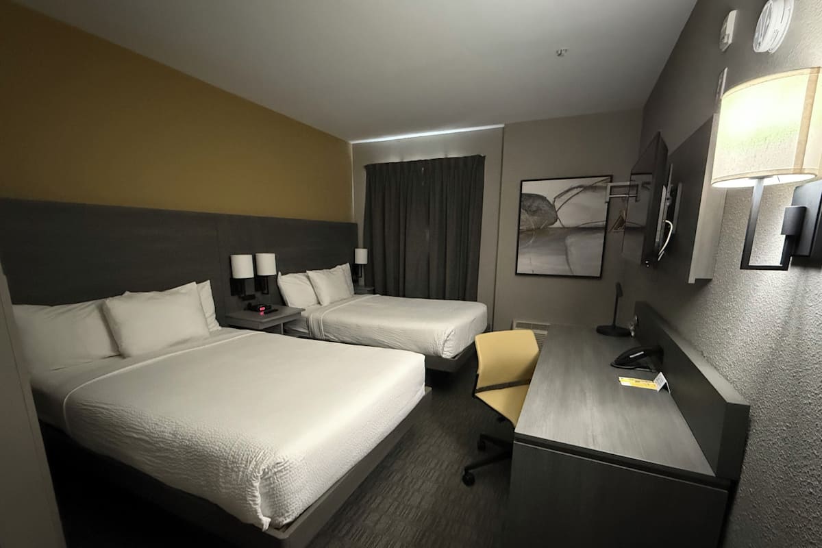A hotel room with two beds, a desk, a chair, a lamp, and a painting on the wall.