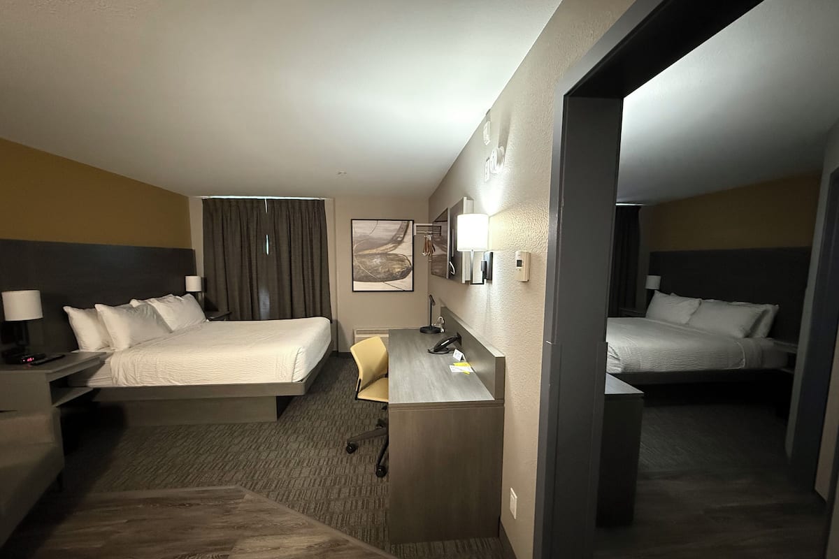 A hotel room with two beds, a desk, a chair, a lamp, and a painting on the wall.