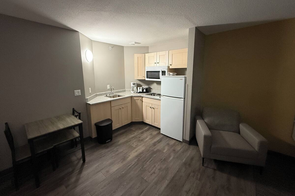 A compact kitchen with a microwave, stove, and refrigerator. There is a small dining table and a chair.