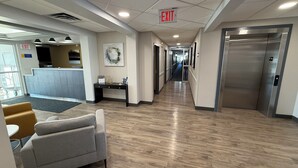 A hotel lobby with a reception desk, a gray sofa, an exit sign, and a hallway leading to elevators. - Days Inn by Wyndham Stony Plain (Stony Plain)