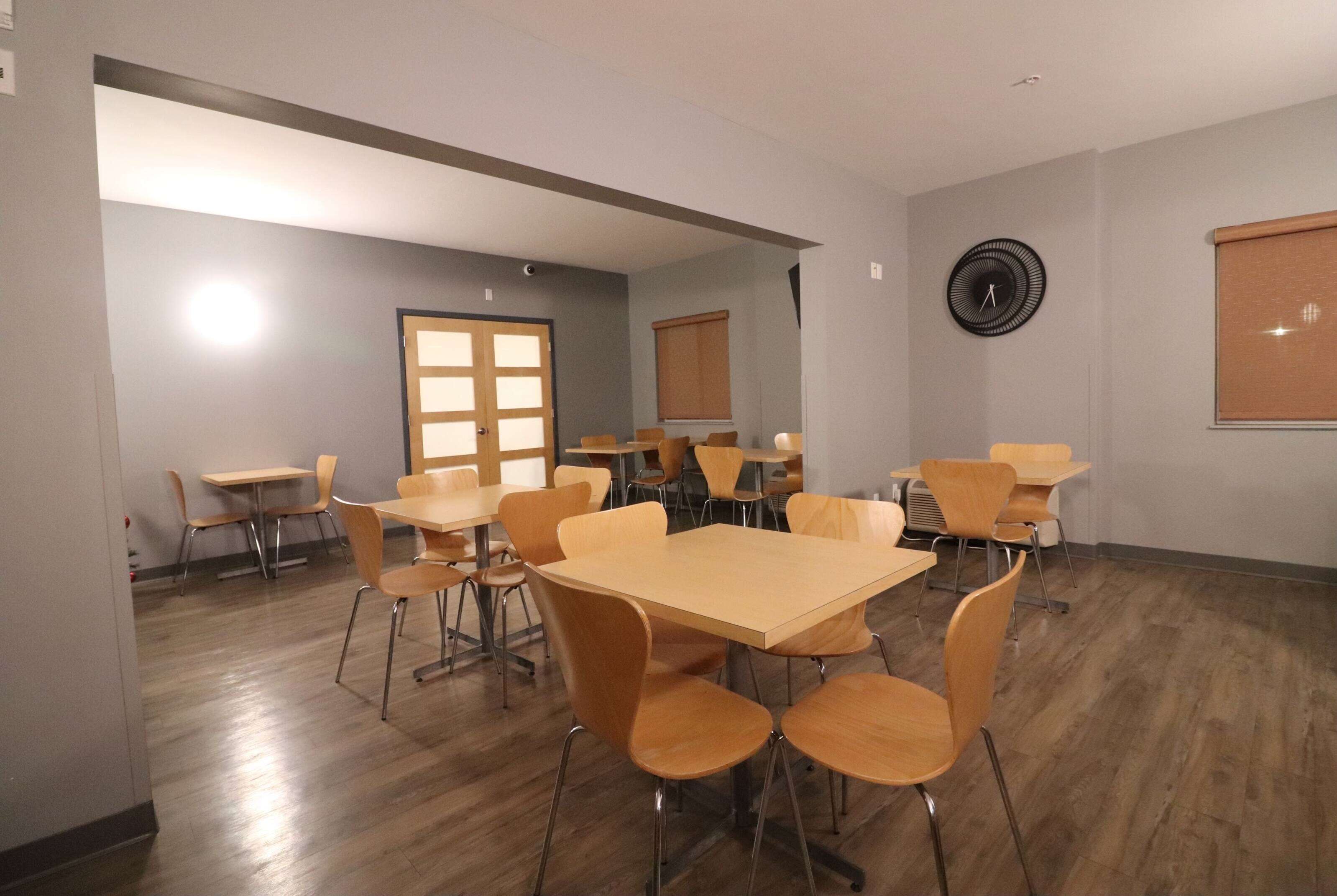 A conference room with multiple tables and chairs, a clock on the wall, and a window with blinds.