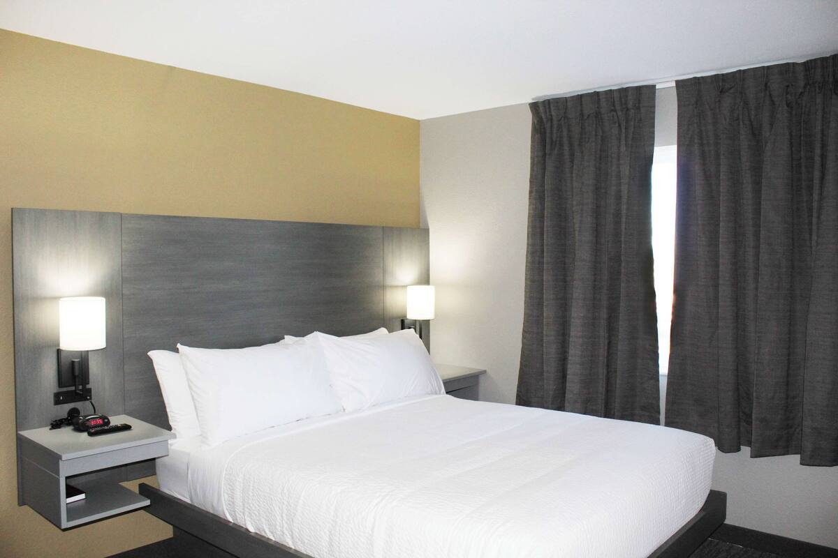 A hotel room with a large bed, two bedside lamps, a nightstand, and a window with curtains.