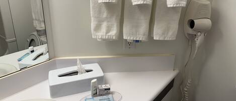 A bathroom with white towels hanging on a rack, a tissue box, a hand sanitizer, and a hair dryer plugged in.