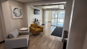 A modern office space with a grey sofa, a mustard-colored armchair, and a small round table. There is a large abstract painting on the wall, a flat-screen TV, and a view through the glass doors to the outside. - Days Inn by Wyndham Stony Plain (Stony Plain)