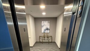 An elevator interior with a herringbone-patterned floor, a wall-mounted abstract artwork, and a small console table with two decorative vases. - Days Inn by Wyndham Stony Plain (Stony Plain)