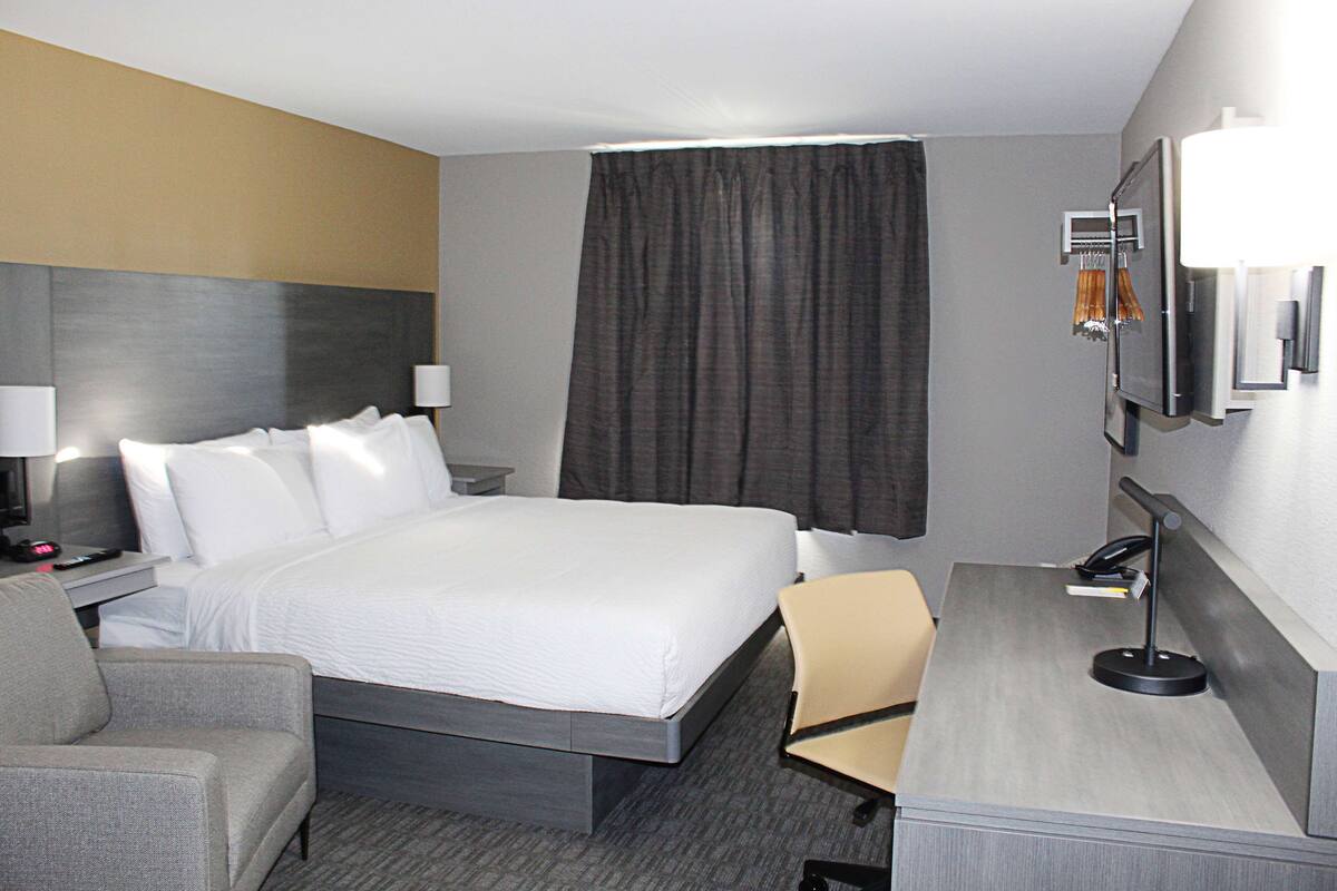 A hotel room with a large bed, a desk, a chair, a lamp, and a TV.