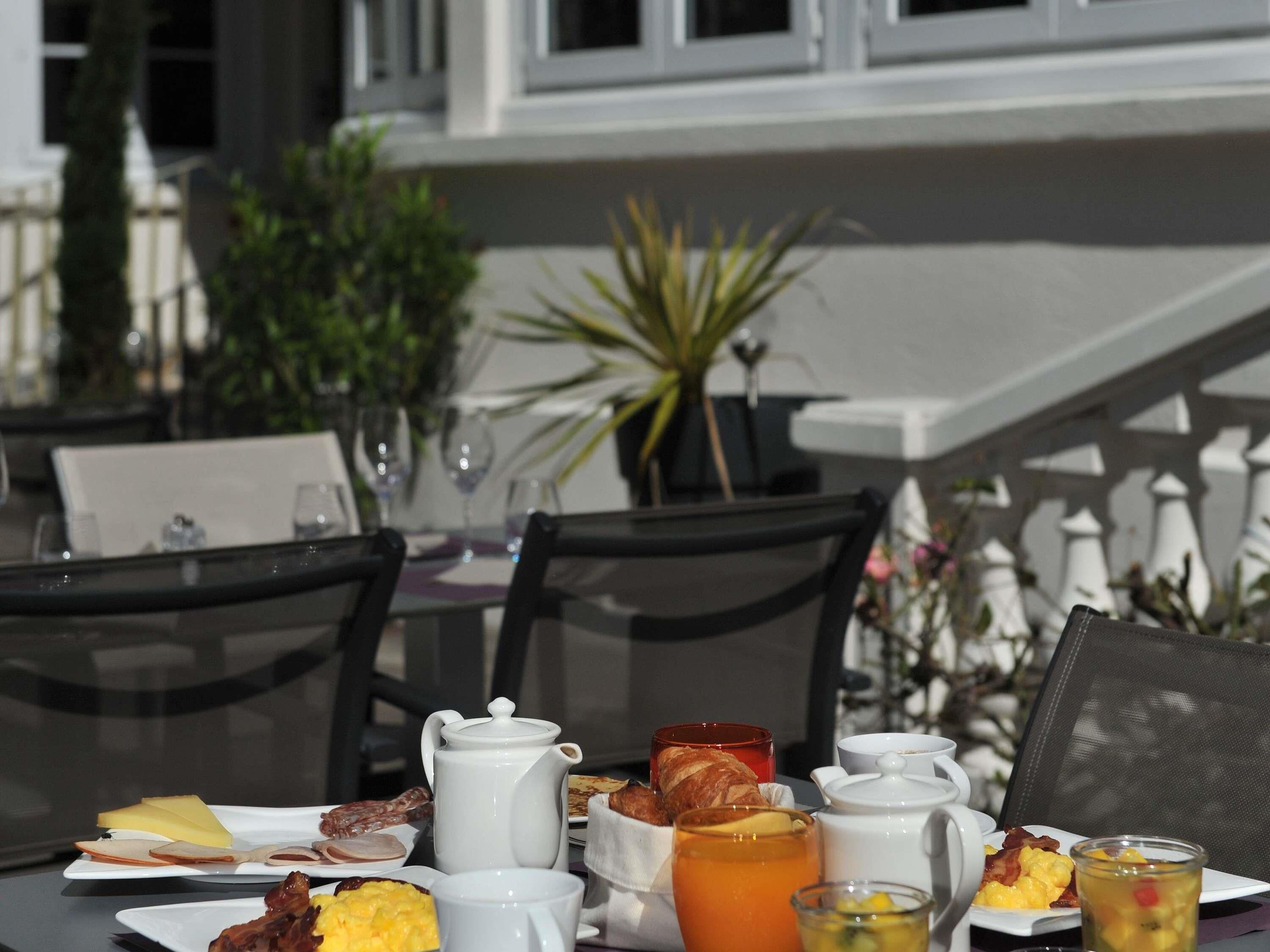 A breakfast table set outdoors with various dishes, a teapot, and cups.