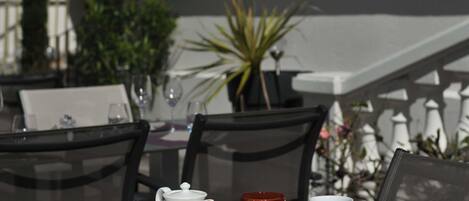 A breakfast table set outdoors with various dishes, a teapot, and cups.