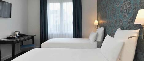 A hotel room with two beds, a desk, a lamp, and a TV.
