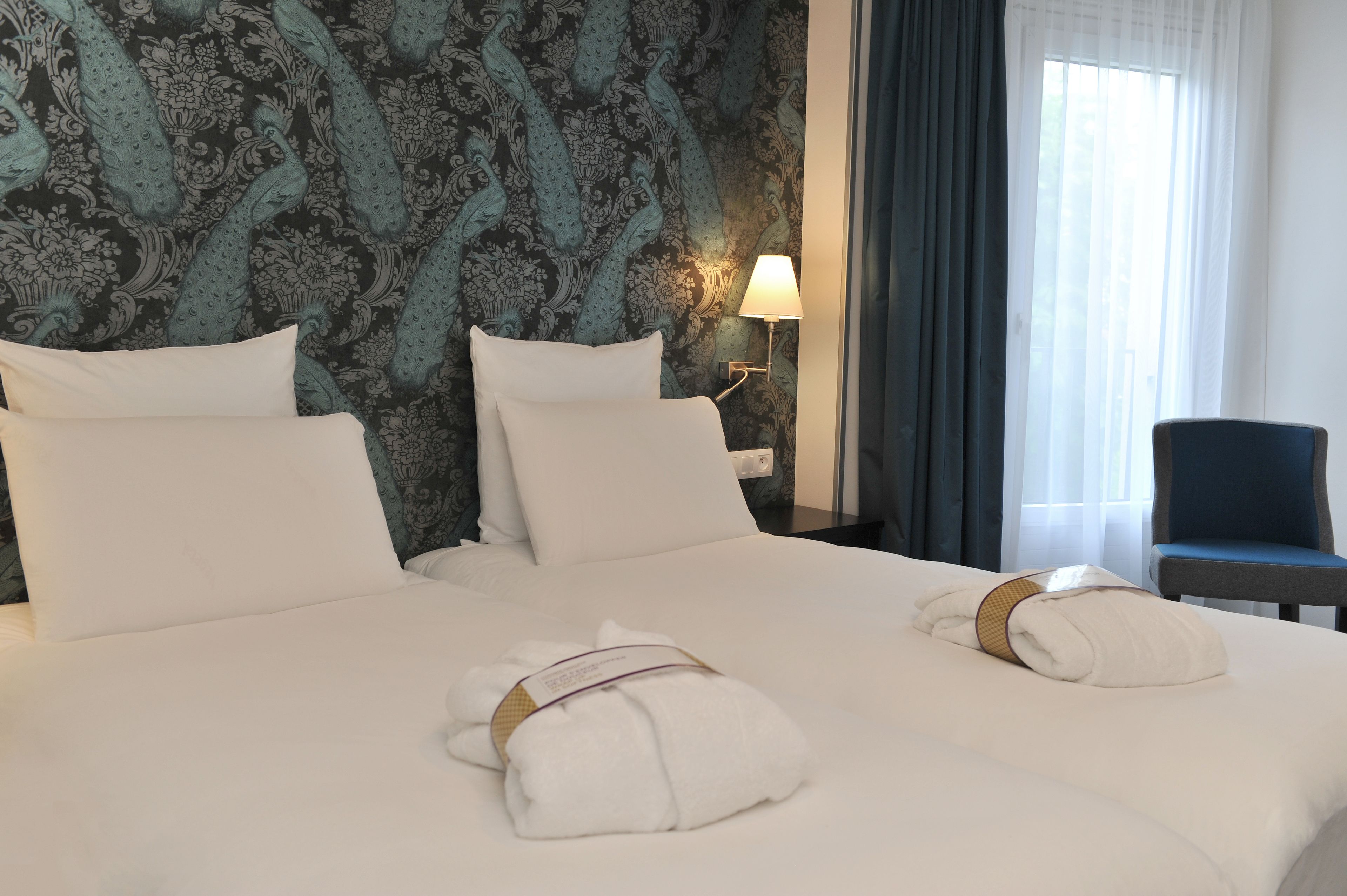 A hotel room with a large bed, two pillows, a nightstand with a lamp, a chair, and towels on the bed.