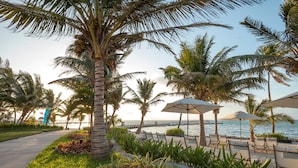 Un resort frente a la playa con palmeras, sillas de descanso y sombrillas.