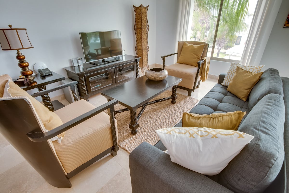 Een moderne woonkamer met een bank, fauteuils, een salontafel, een televisie en een lamp.