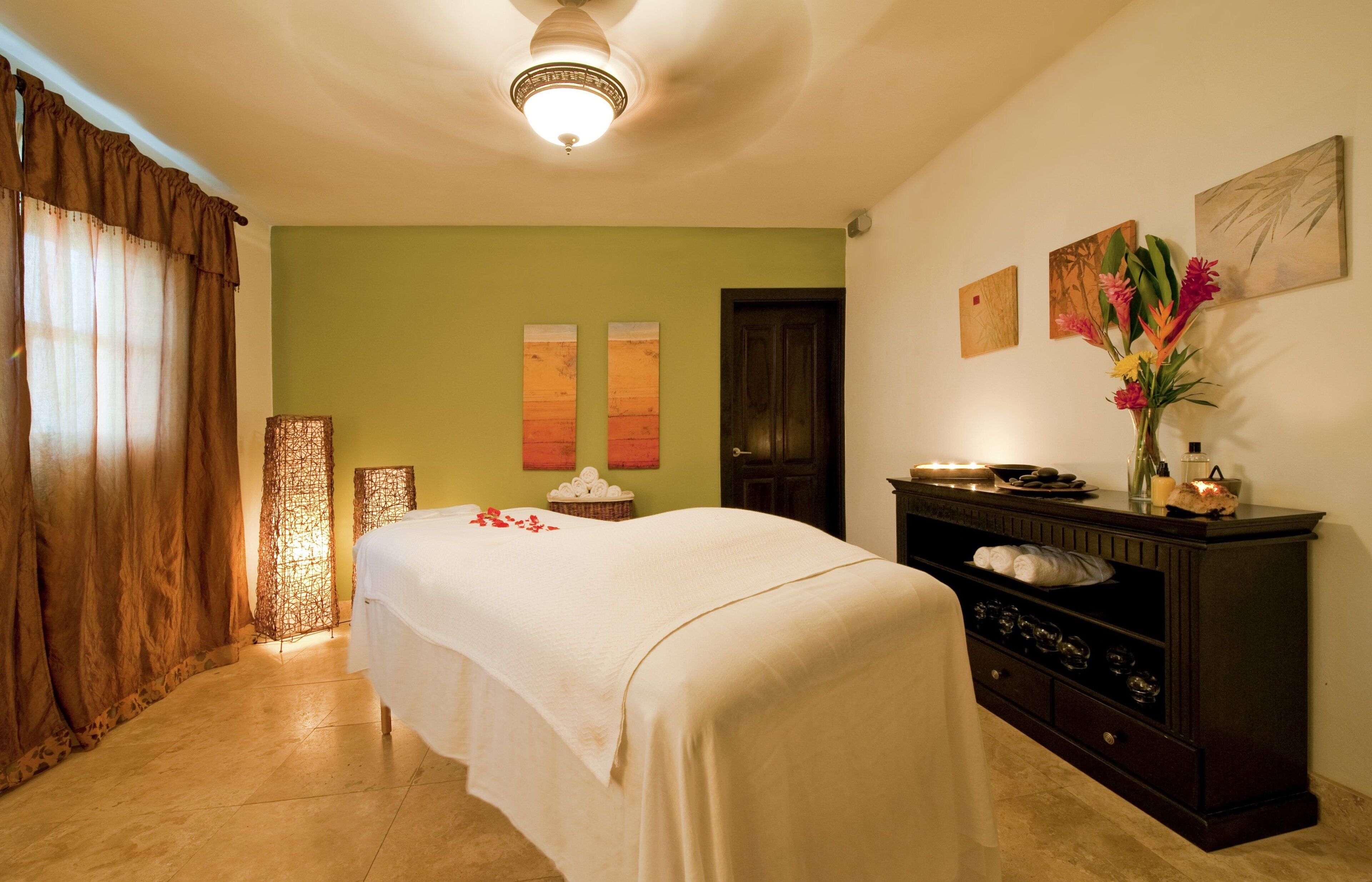 A room with a bed, a wooden dresser, and a wall with three paintings.