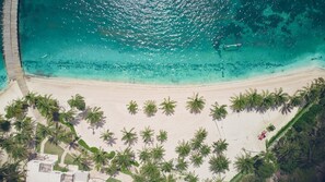 Luchtbeeld van een strand met helder turquoise water, een zandstrand en rijen palmbomen.