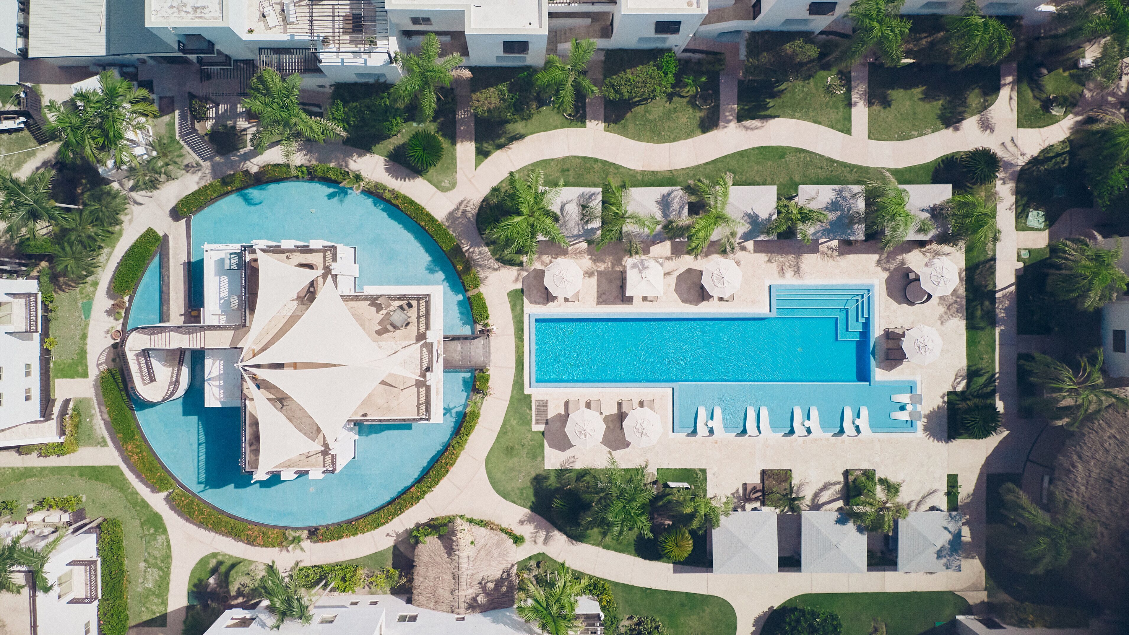 An aerial view of a resort with a large central pool, smaller pools, and sun loungers.