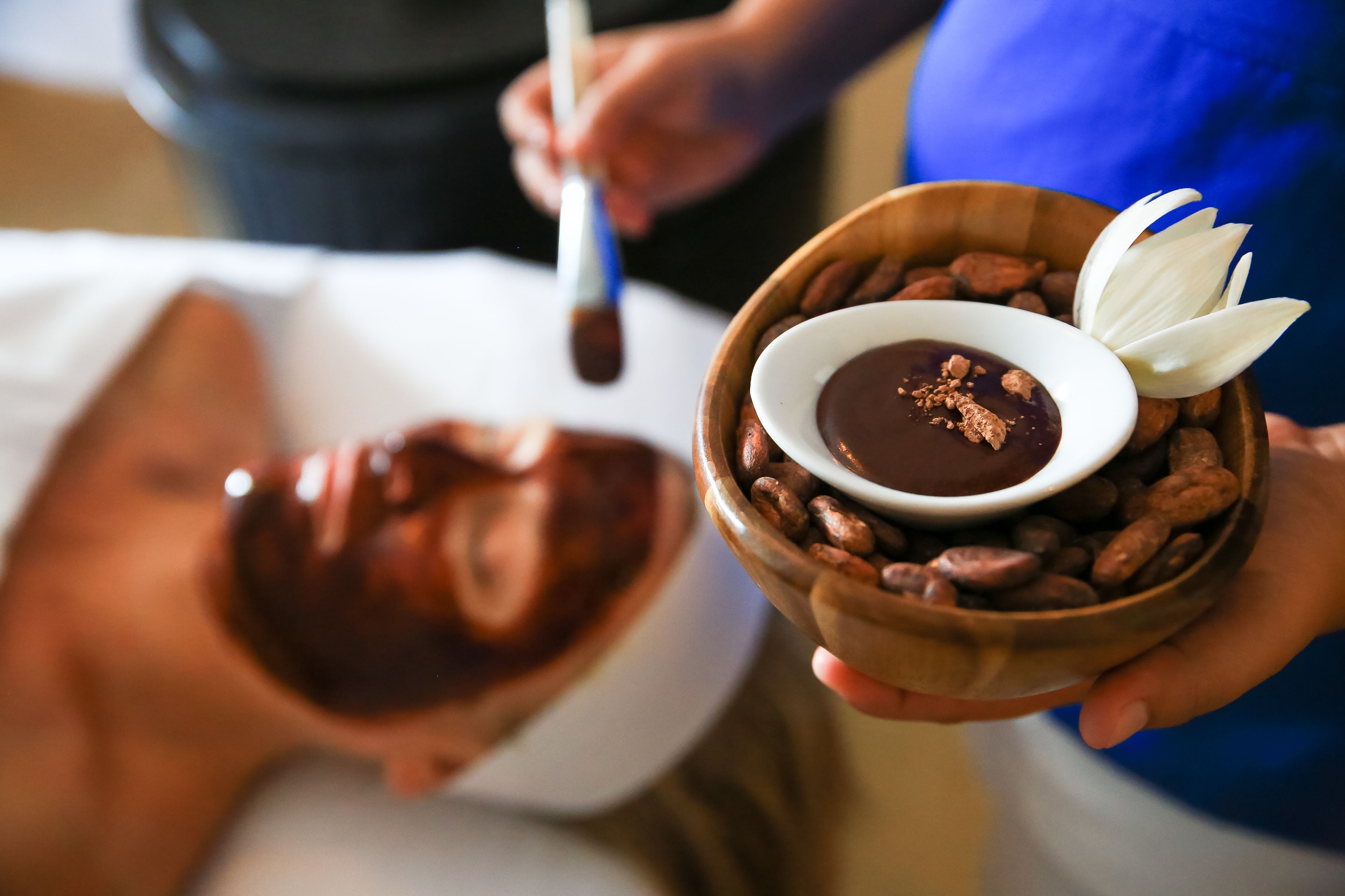 Una persona sosteniendo un tazón de chocolate con una flor y nueces.