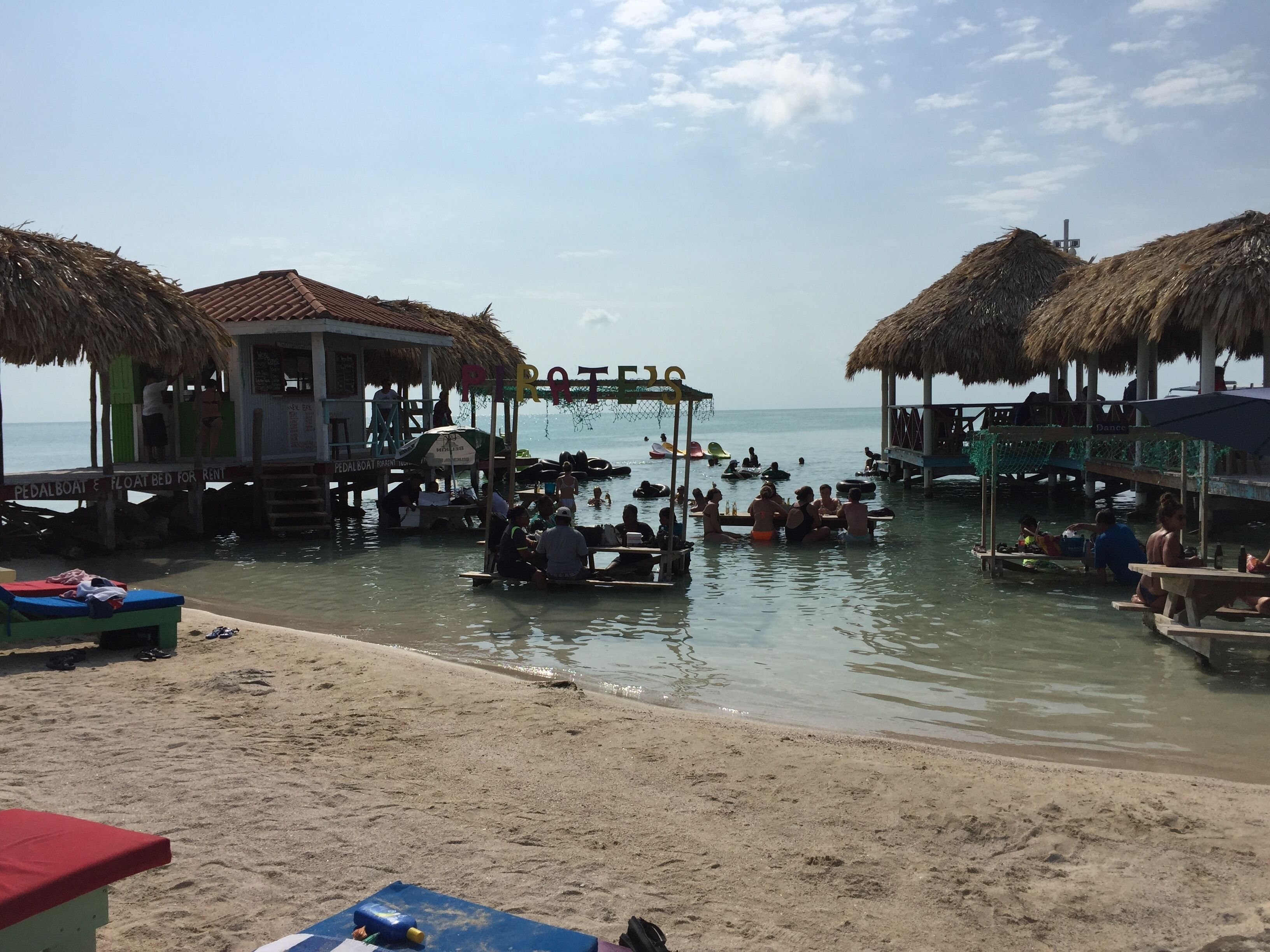 A beachside pier with thatched-roof structures, a sandy beach, and a calm sea.