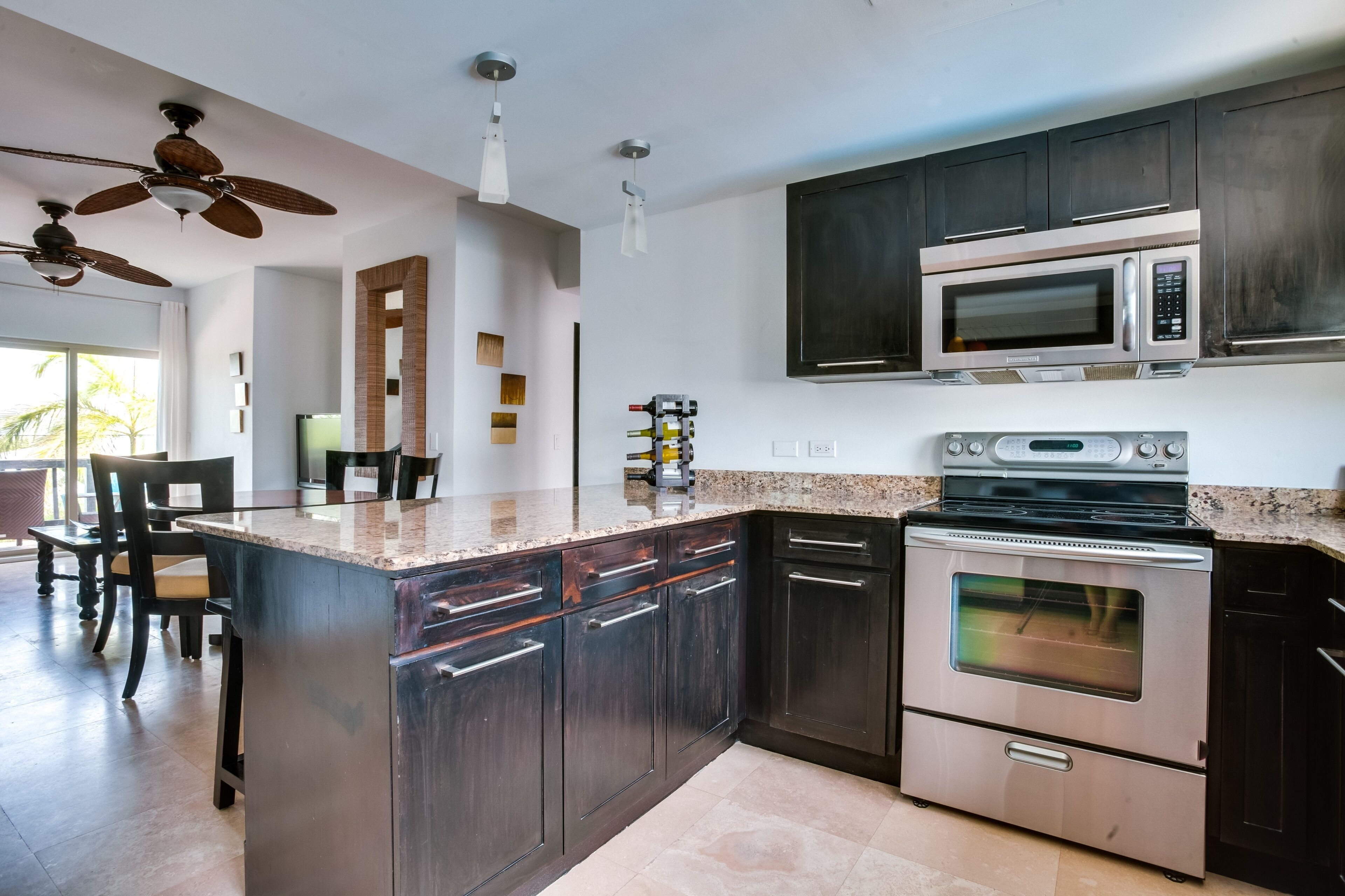 A modern kitchen with dark wooden cabinets, stainless steel appliances, a granite countertop, and a ceiling fan.