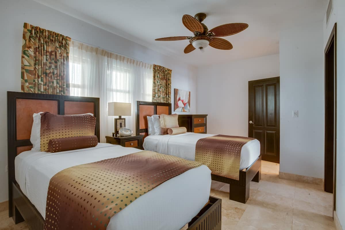 Een hotelkamer met twee bedden, een plafondventilator en een deur.