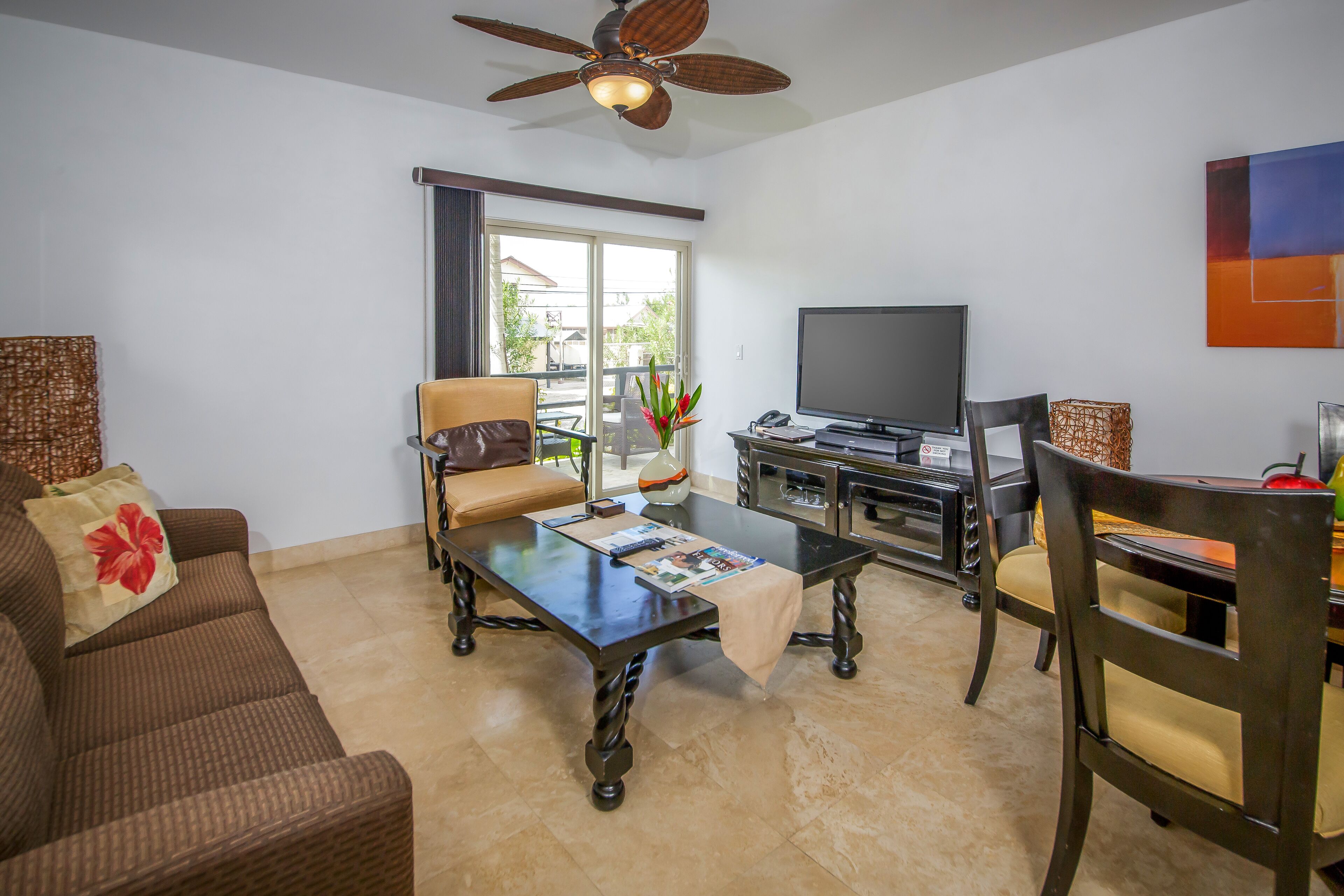 A living room with a sofa, armchair, coffee table, TV, and a ceiling fan.