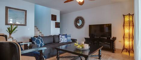 Una sala de estar moderna con sofá, mesa de centro, televisor y elementos decorativos.
