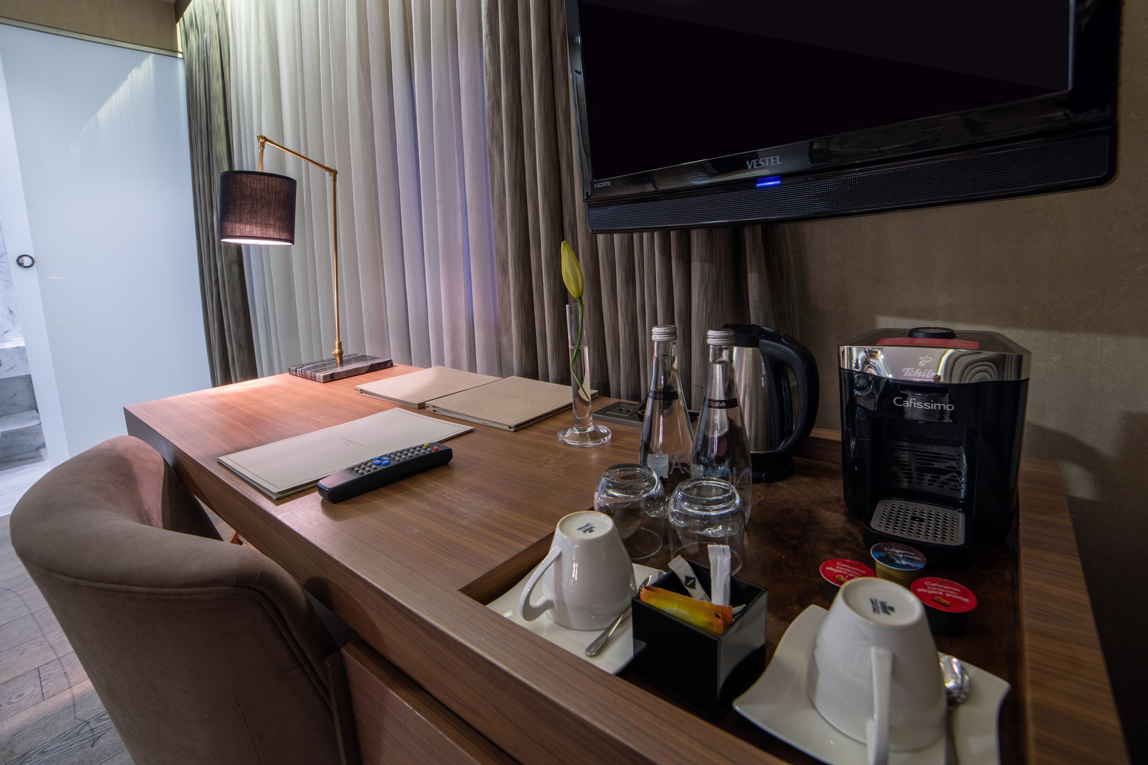 Habitación de hotel con un escritorio de madera, un televisor, una cafetera y un control remoto.