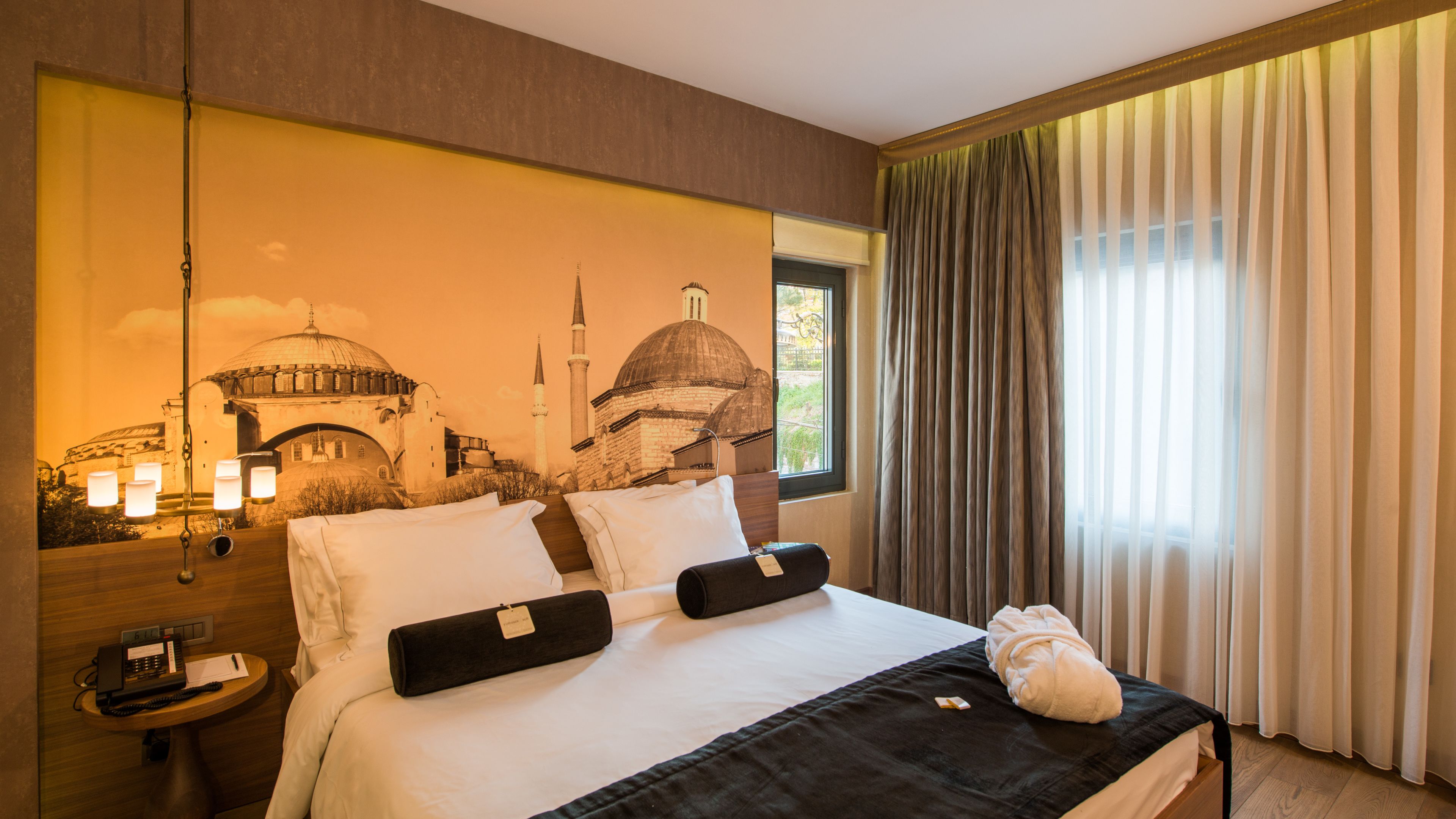 A hotel room with a large bed, a nightstand with a phone, and a wall-mounted lamp.