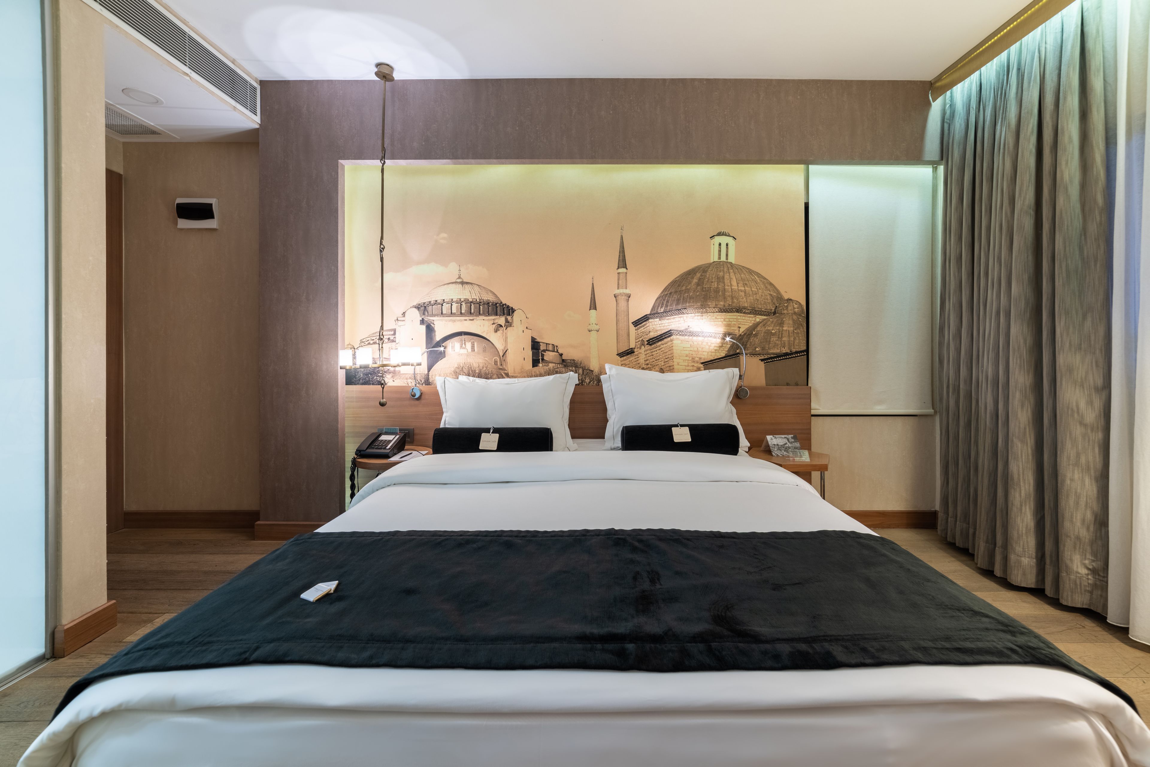 A hotel room with a large bed, a nightstand, and a wall mural of a cityscape.