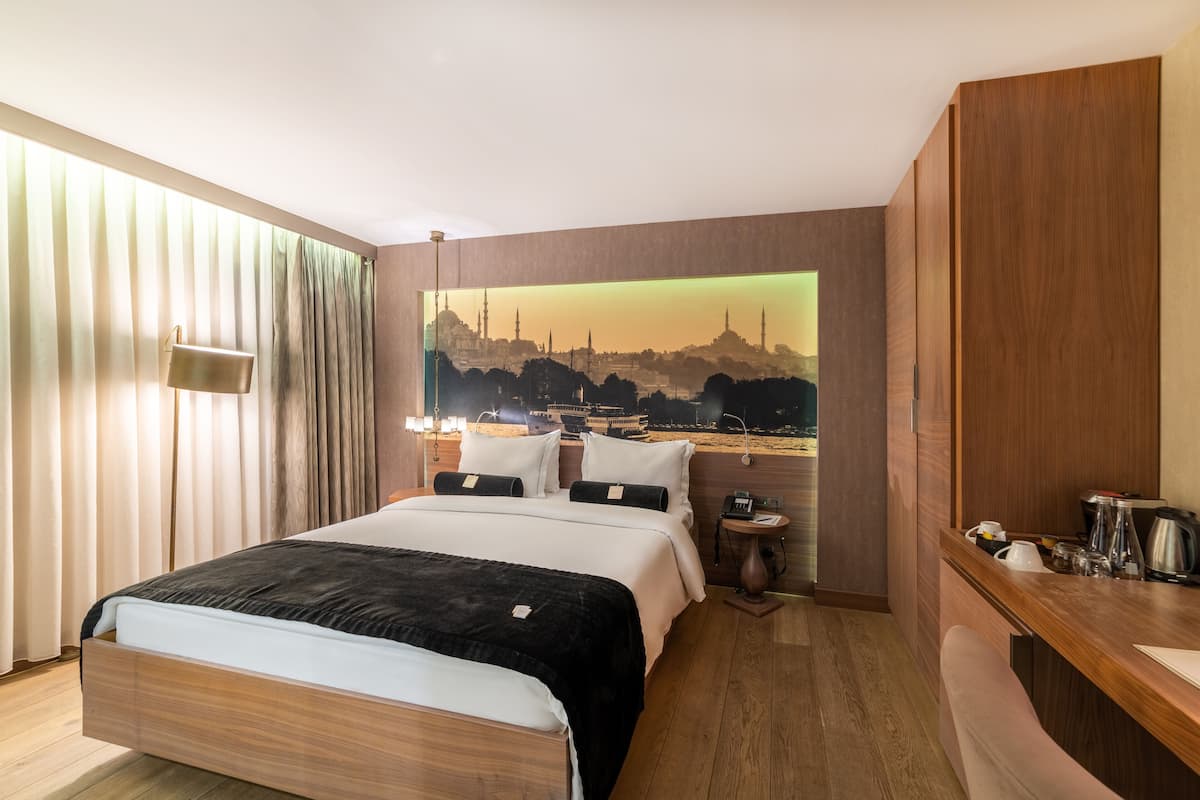 Une chambre d’hôtel avec un grand lit, une table de chevet, une commode et une vue sur le paysage urbain.