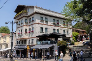 A multi-story building with a restaurant on the ground floor, balconies with flower boxes, and a pedestrian area with people walking. - Hotel Saint Sophia (Istanbul)