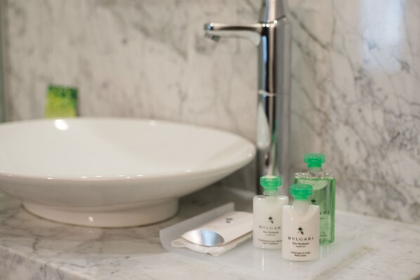A bathroom with a white sink, a mirror, and two bottles of BVLGARI body lotion on the marble countertop.
