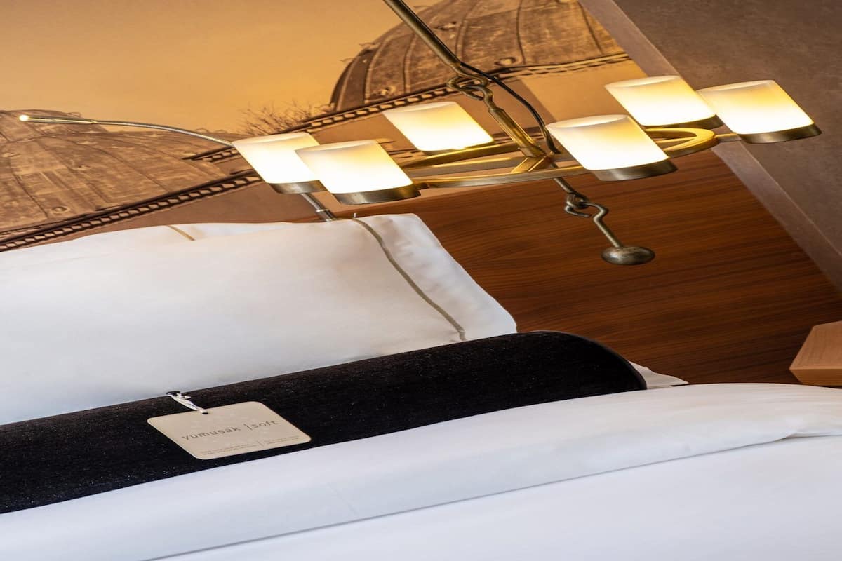 Une chambre d’hôtel avec un lit, une table de chevet et une lampe fixée au mur.
