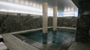 Un espace spa doté d’une piscine rectangulaire, de murs en pierre et d’un coin salon avec un coussin blanc.