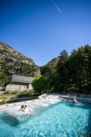 Una piscina con agua azul cristalina, rodeada de zona boscosa y una montaña rocosa al fondo.