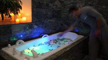 Un hombre en un entorno tipo spa con una bañera grande llena de peces, rodeado de una pared de piedra oscura y una planta.