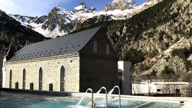 Une piscine avec un bâtiment en pierre en arrière-plan, entourée de montagnes.