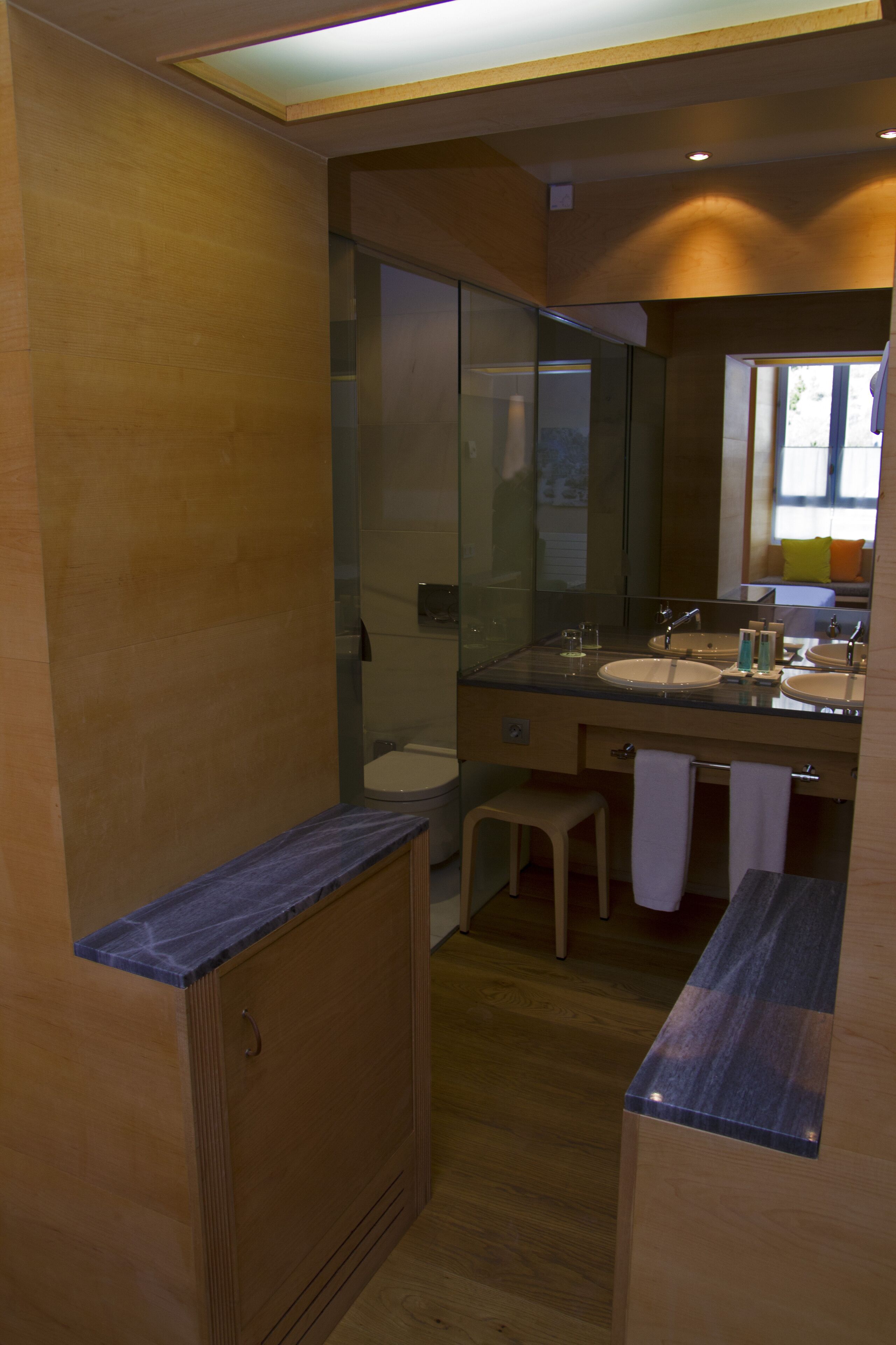 Ein modernes Badezimmer mit Holzschränken, einer Duschkabine aus Glas und einem Waschtisch mit zwei Becken und einem Spiegel.