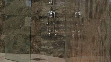 A modern bathroom with a glass-enclosed shower, marble walls, and a row of candles along the floor.