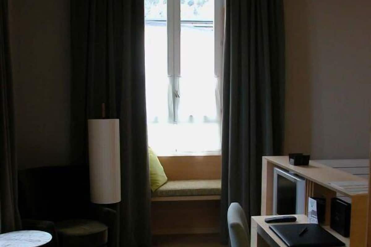 Une petite pièce, de taille modeste, comprenant un bureau, une chaise et une fenêtre donnant sur l’extérieur.