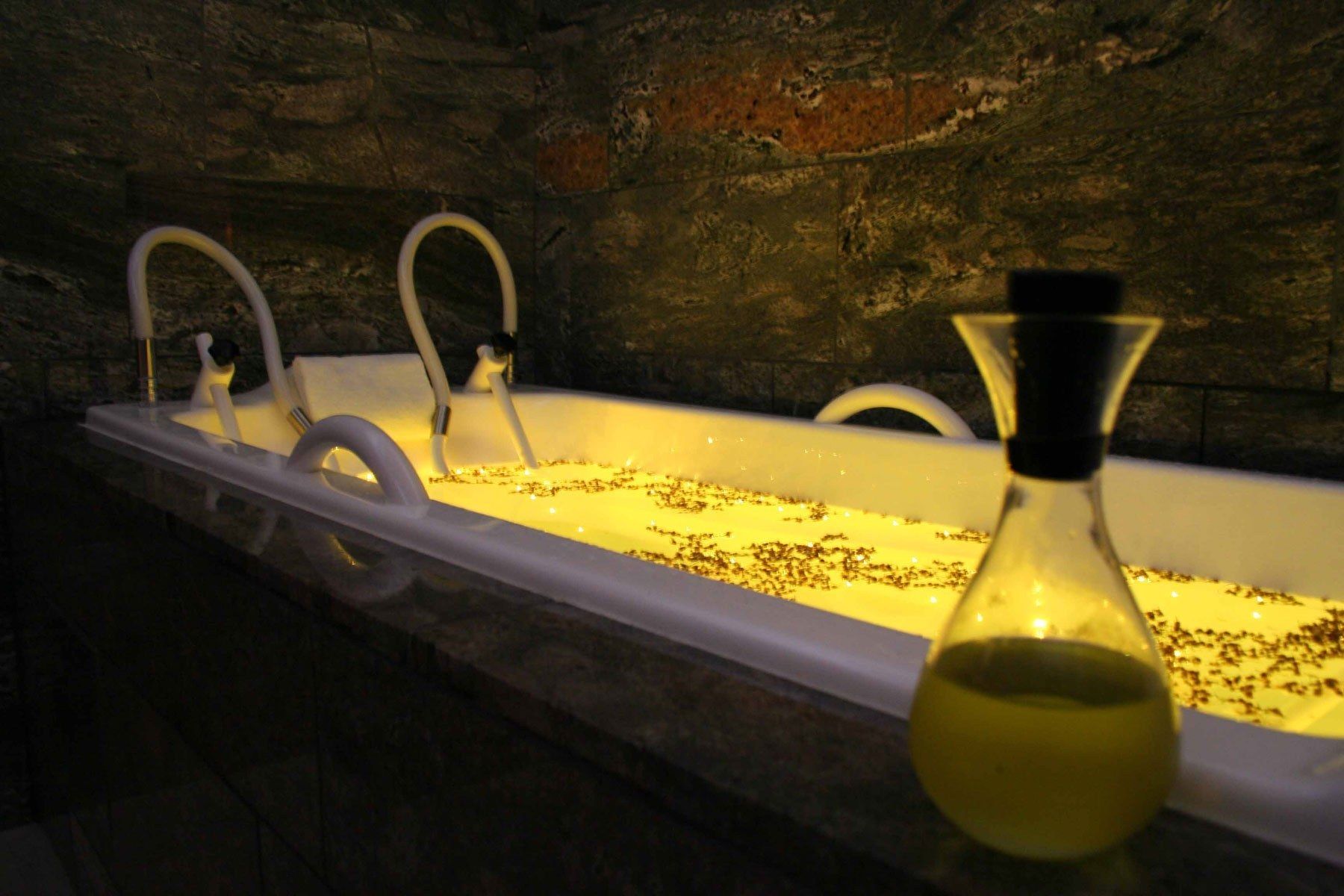A bathtub with a glass enclosure, a bottle of oil, and two faucets.