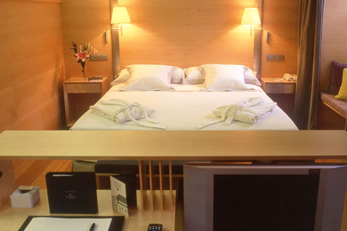 Une chambre d’hôtel comprenant un lit, deux lampes de chevet, une table de chevet avec un vase de fleurs, un bureau avec un ordinateur et une télévision.