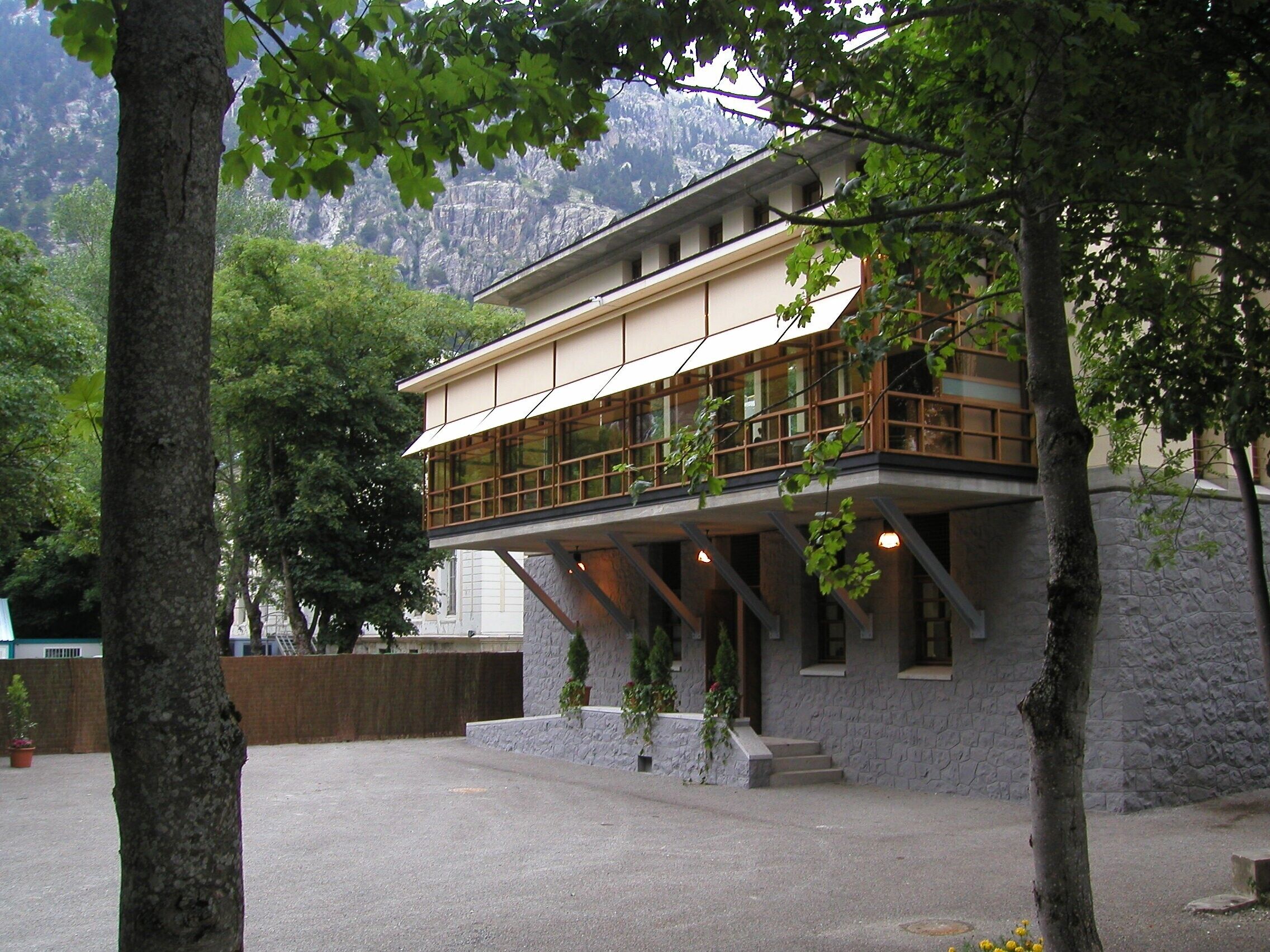 Un edificio di due piani con un balcone, pareti in pietra e montagne sullo sfondo.