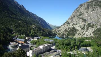 A mountainous landscape with a lake, surrounded by dense forests and steep cliffs. There are buildings with modern architecture, including a large complex with multiple buildings and a parking area.
