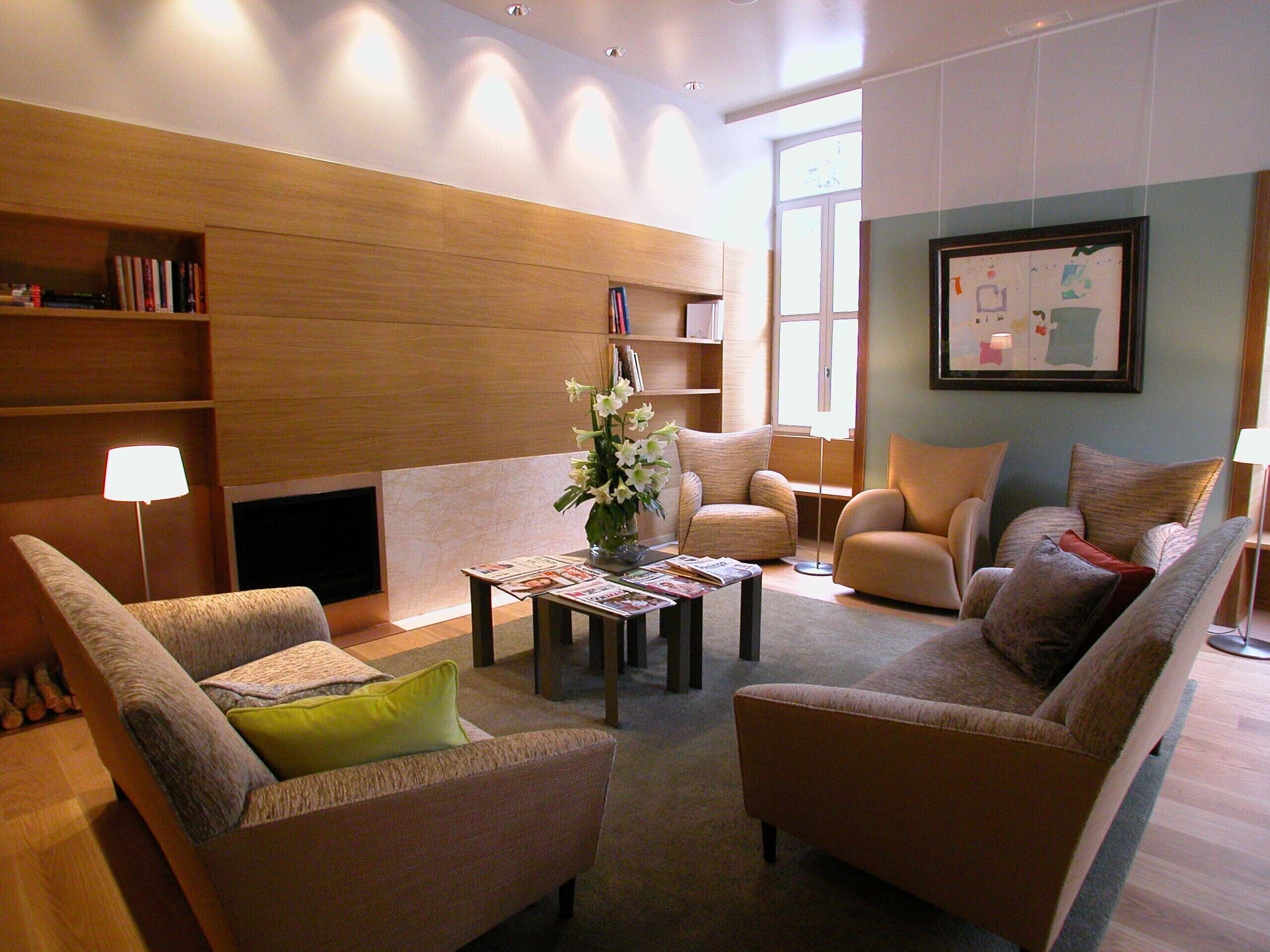 Un salon moderne avec une cheminée, des fauteuils confortables, une table basse avec des magazines et une bibliothèque.